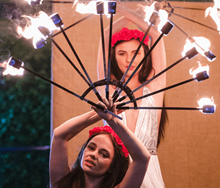 Two women holding sticks of fire above their heads as part of a BNU Festiball student event