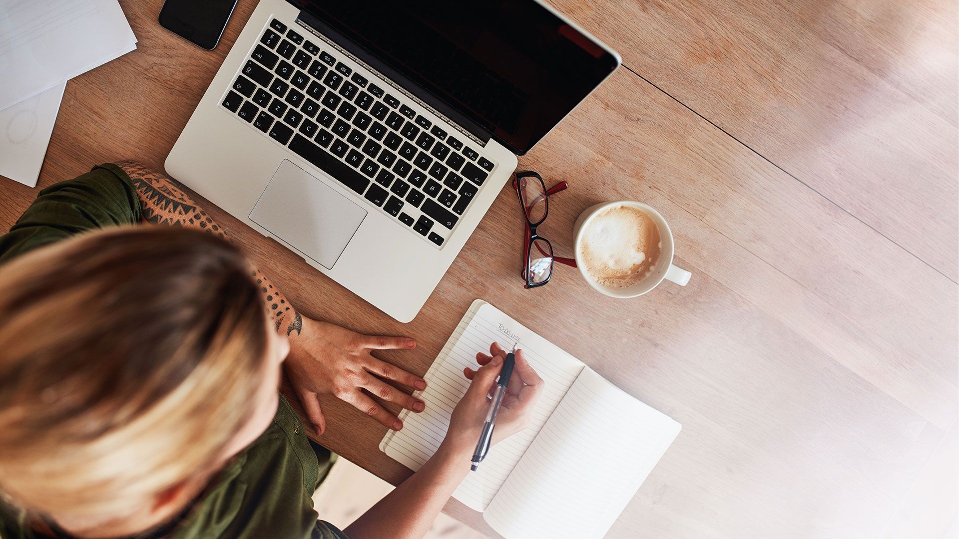 aerial view of a woman sat at a table making notes next to her laptop