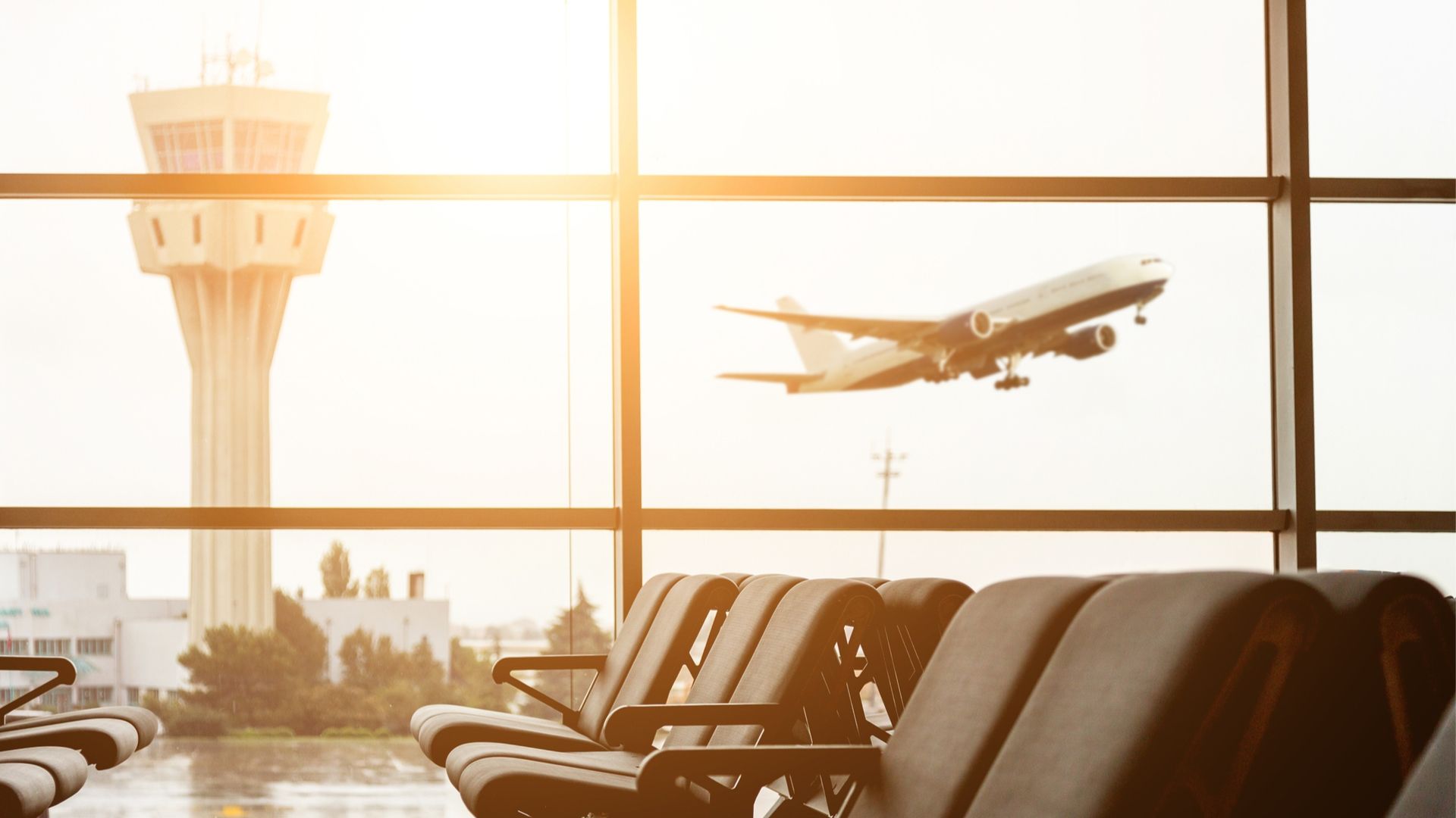 Inside of an airport looking out onto the runway and seeing a plane take off