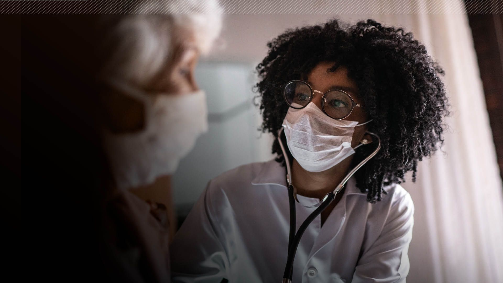 A nurse with a mask and glasses on attends to a patient