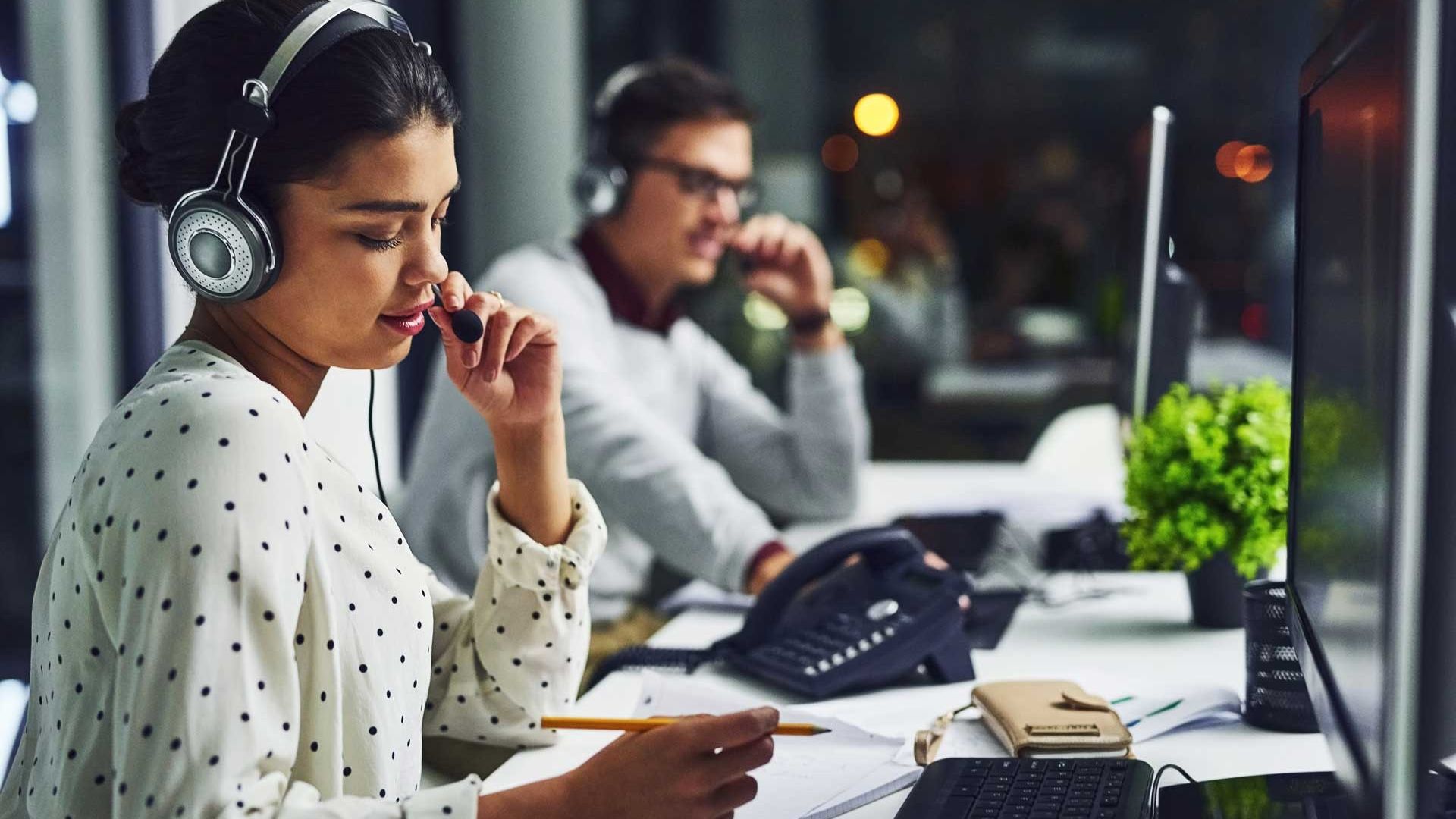 Female on headset phone writing down notes. Man in background on phone