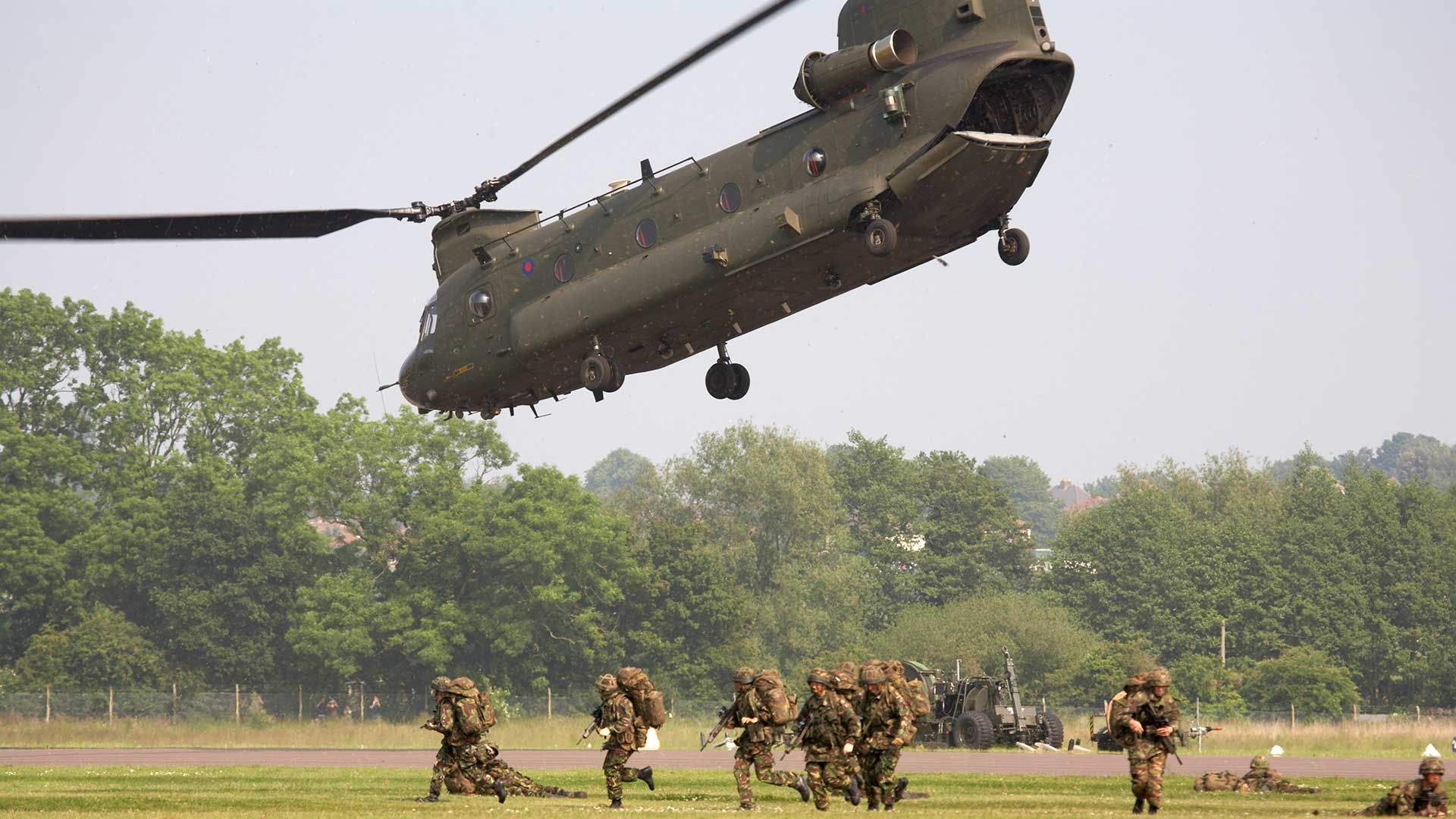 Military chinook flying with soldiers on the ground ready to disperse 