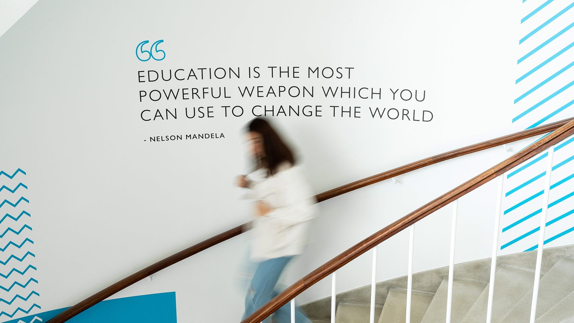 student walking down the stairs in the Gateway building in front of a Nelson Mandela quote