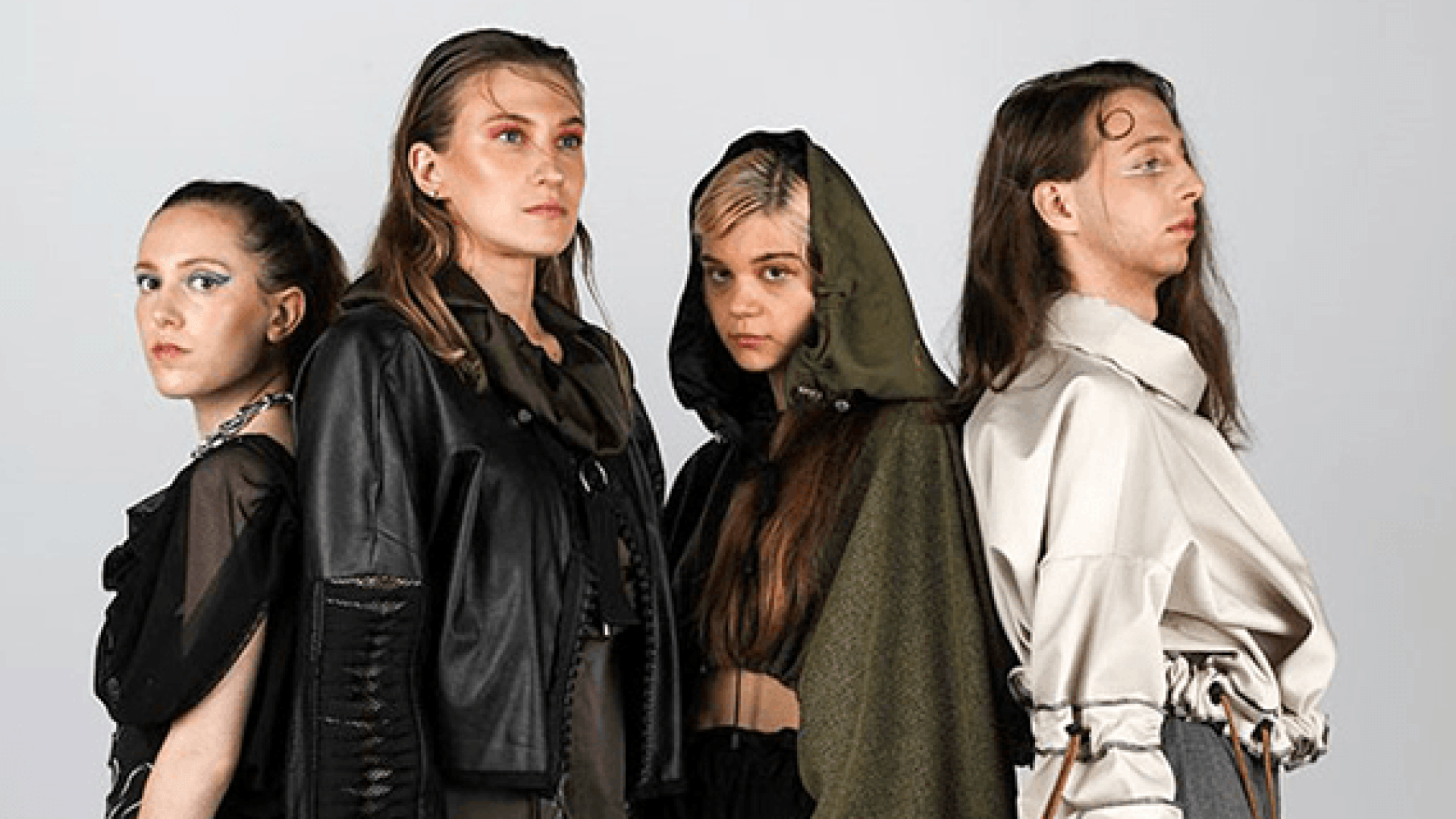 Four Fashion Design students stood posing back to back for a photoshoot against a grey wall
