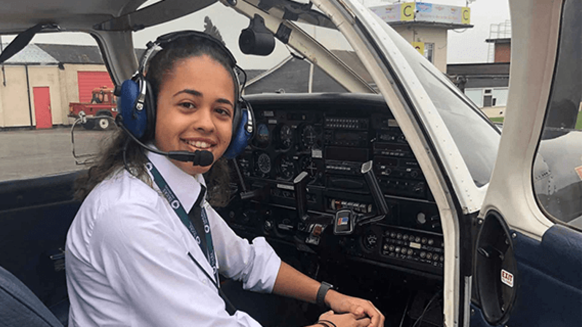 A BNU Commercial Pilot Training student sat in the cockpit of a plane smiling towards the camera