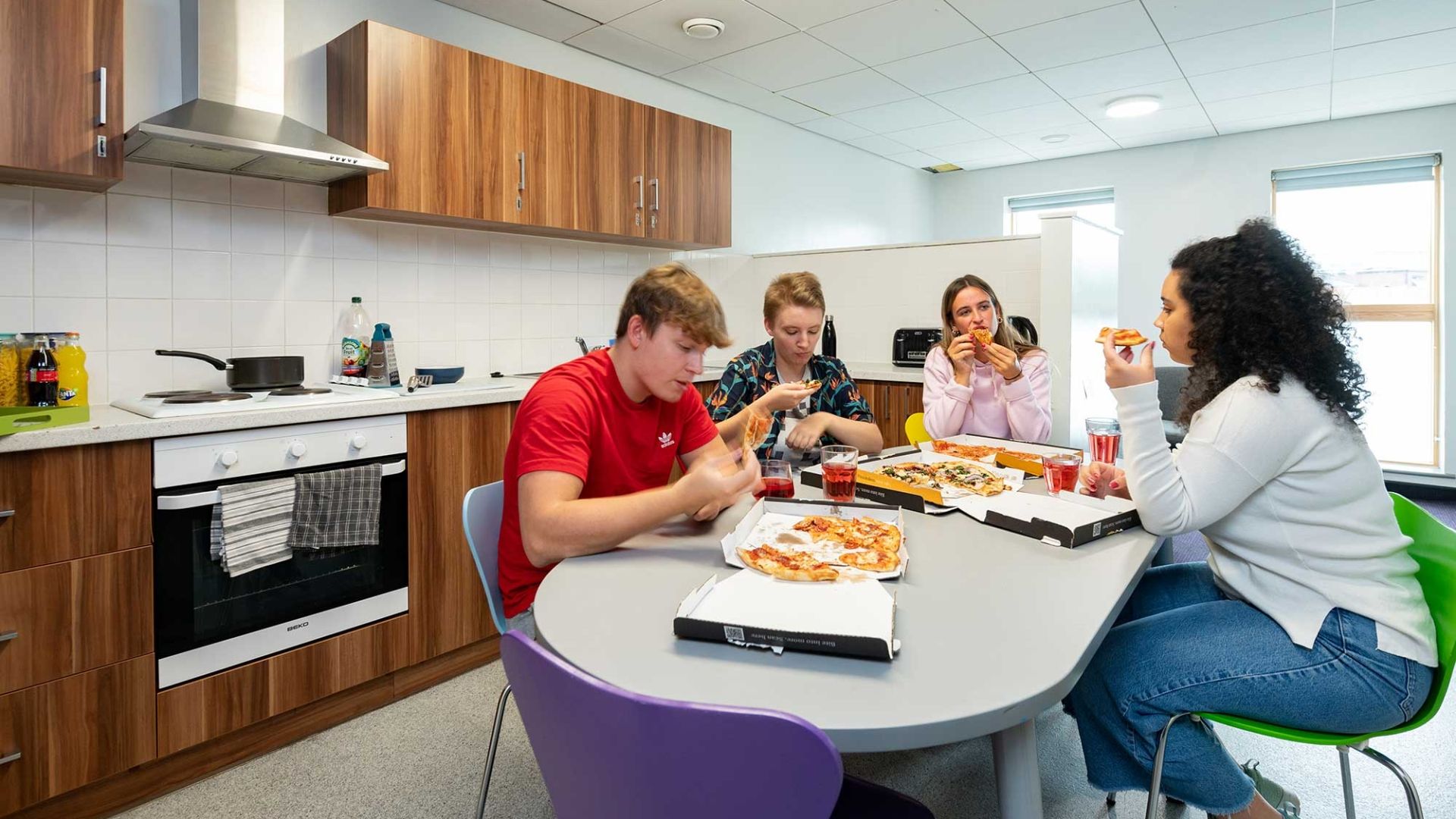 four students eating pizza at a kitchen table in Windsor House accommodation