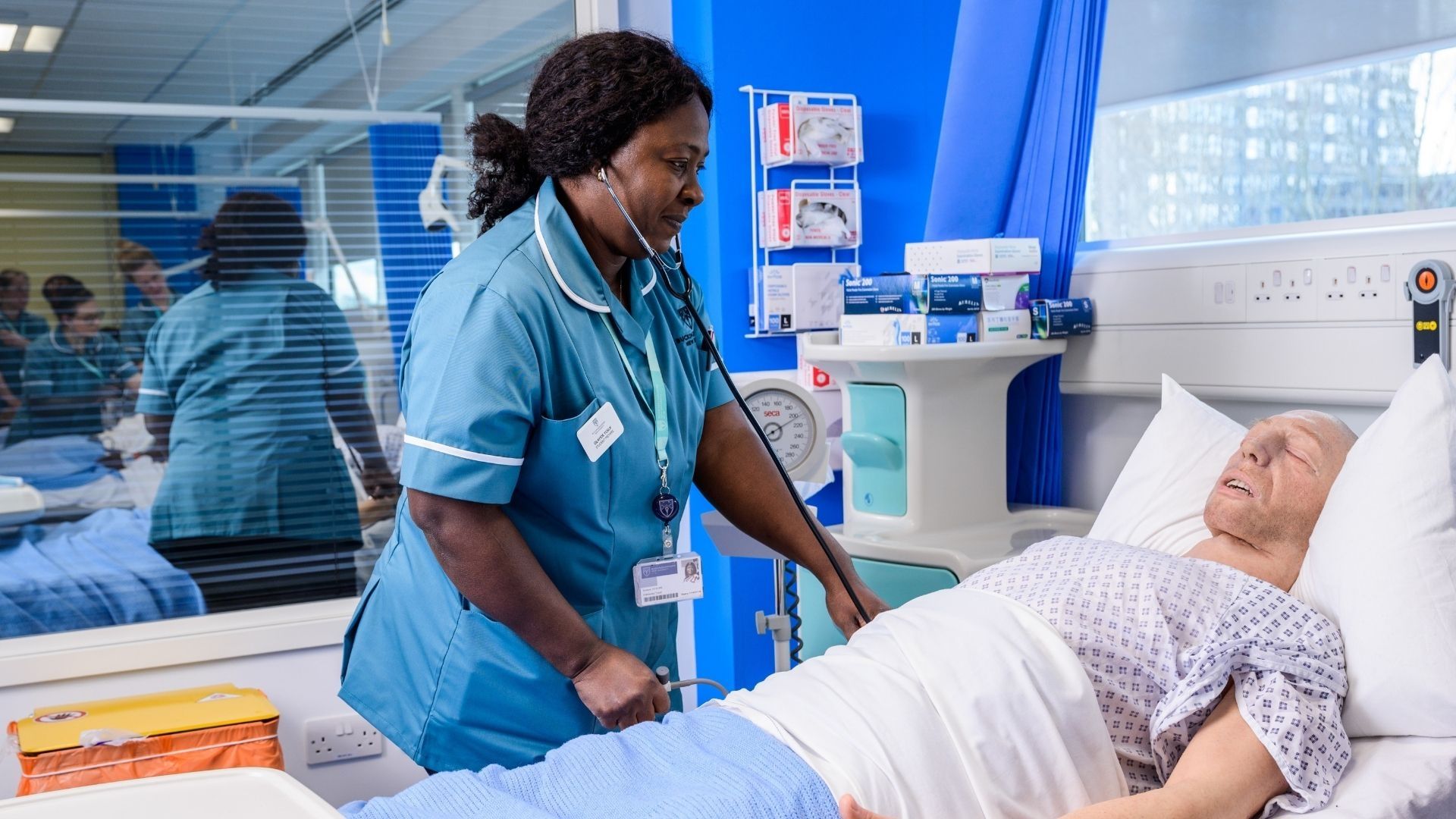 A Nursing student stood up leaning of a hospital bed which has a male dummy in it