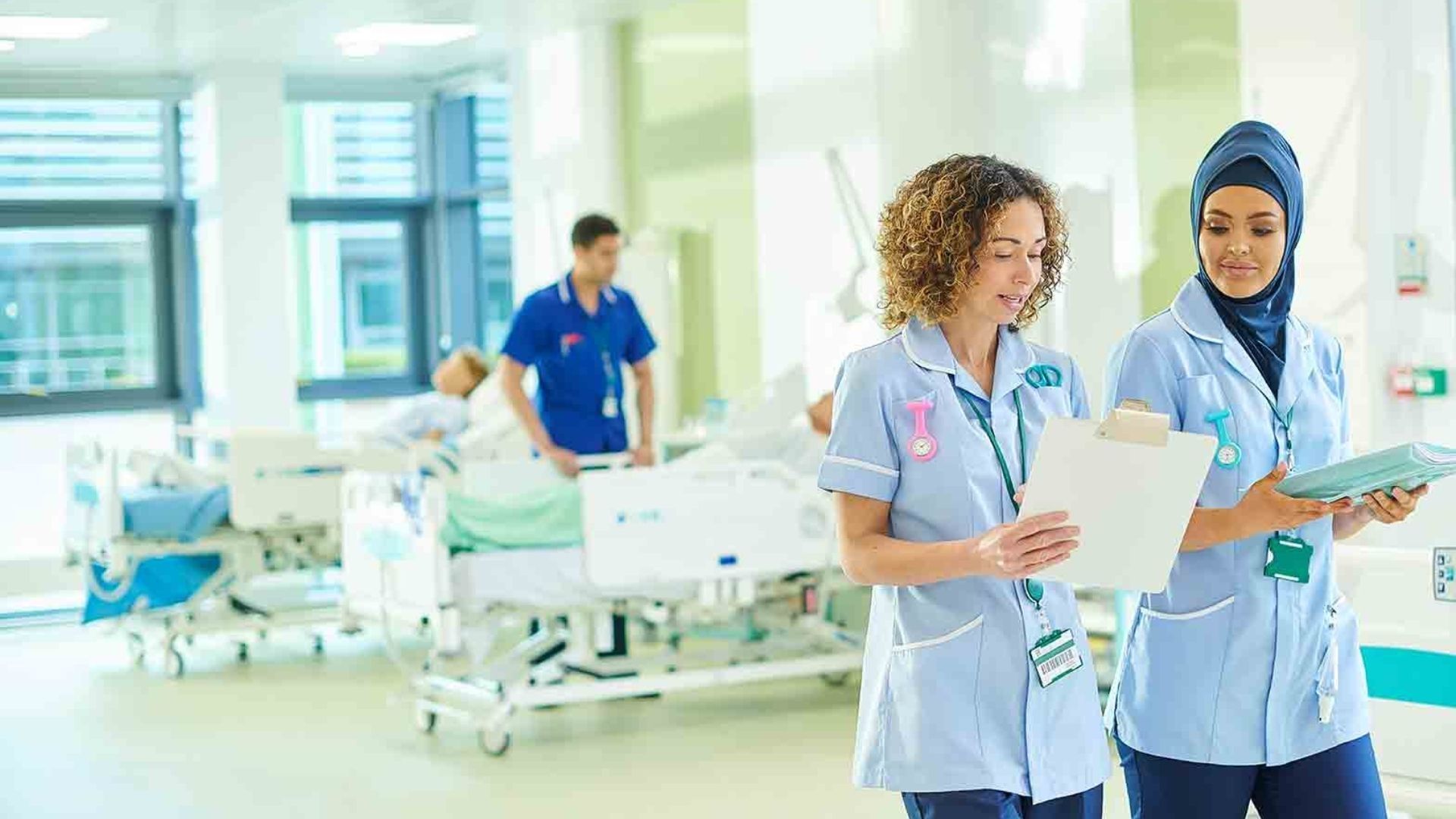 Two female nursing students looking at a clip board whilst walking through a hospital ward