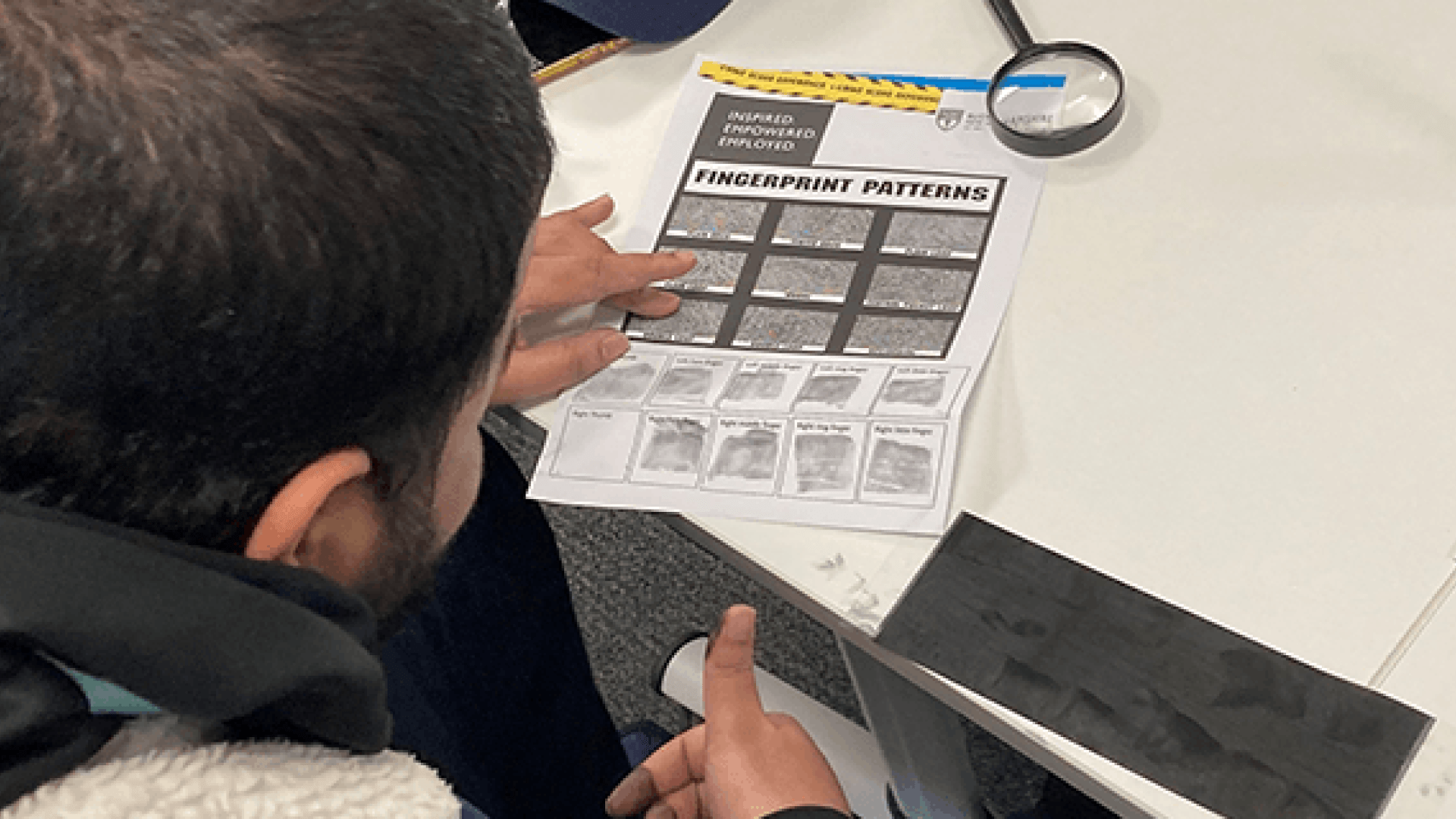 A Criminology student sat at a desk putting his finger print onto a piece of paper