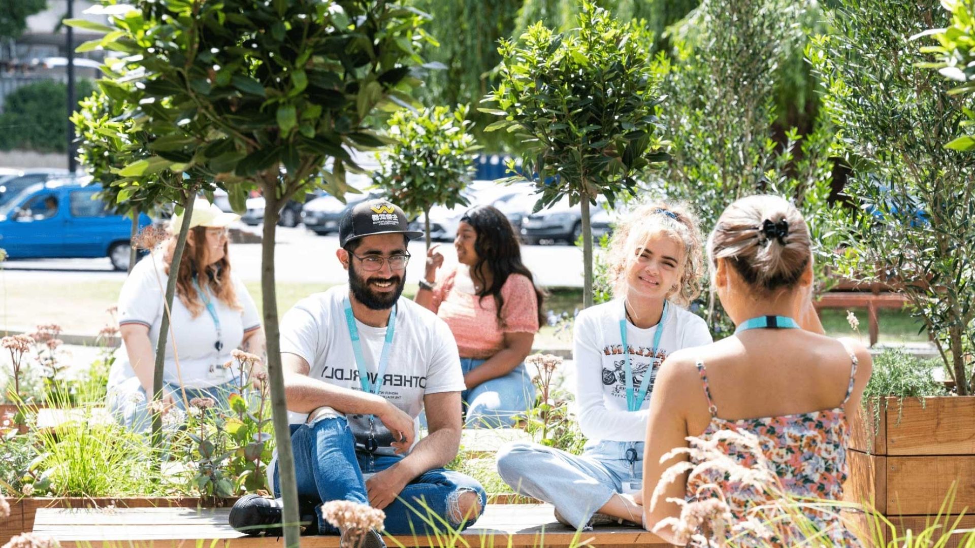Five BNU students sat on wooden benches in amongst trees on concourse in the sunshine