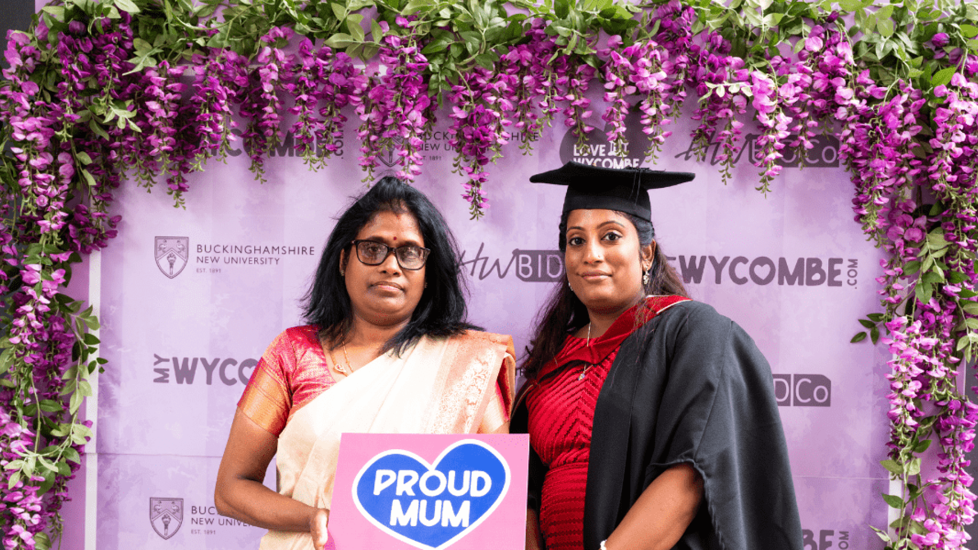 A mum stood with her daughter under some flowers on graduation day