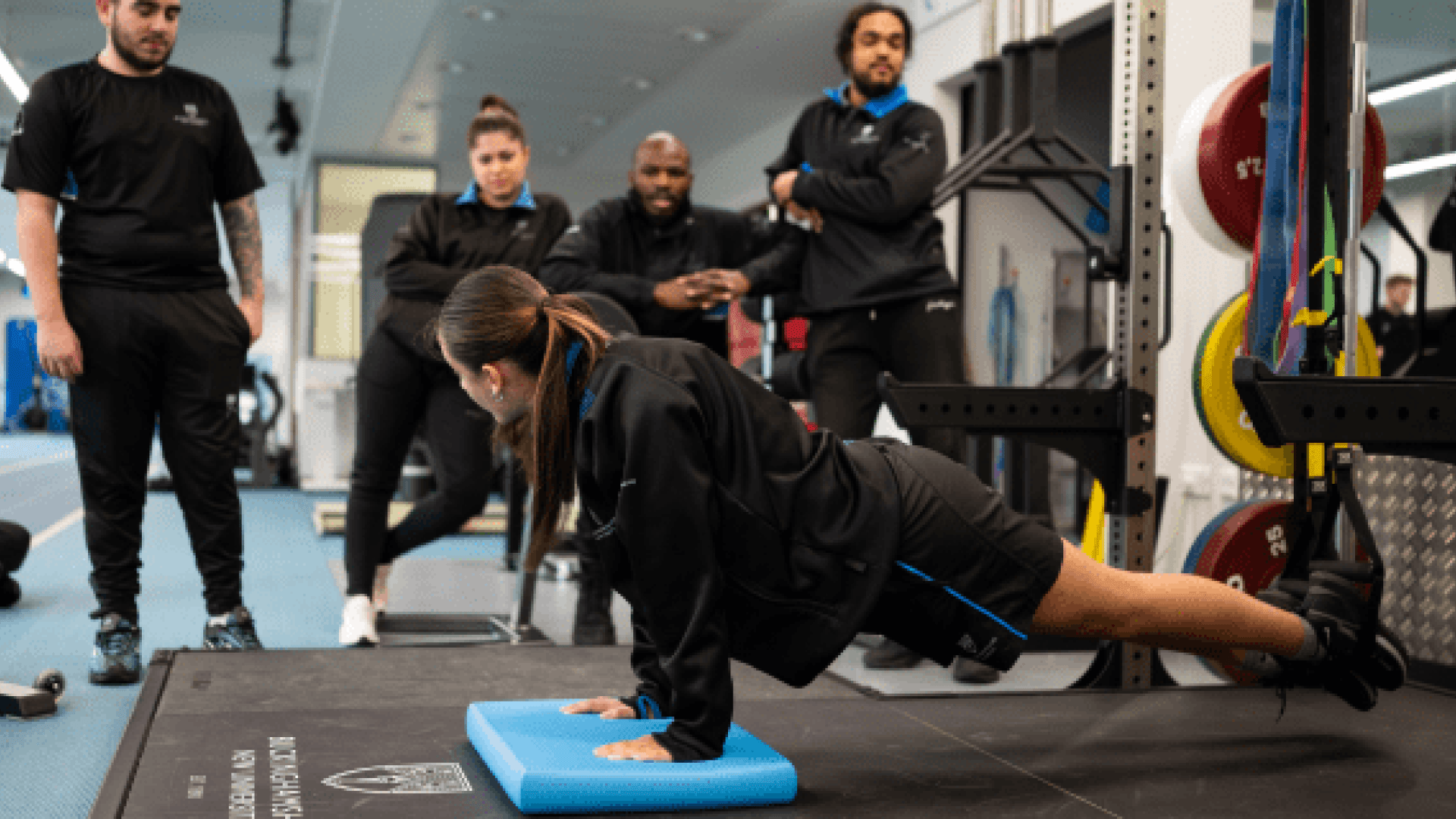 A Sports Therapy student doing a press up on the floor as four other students watch on.
