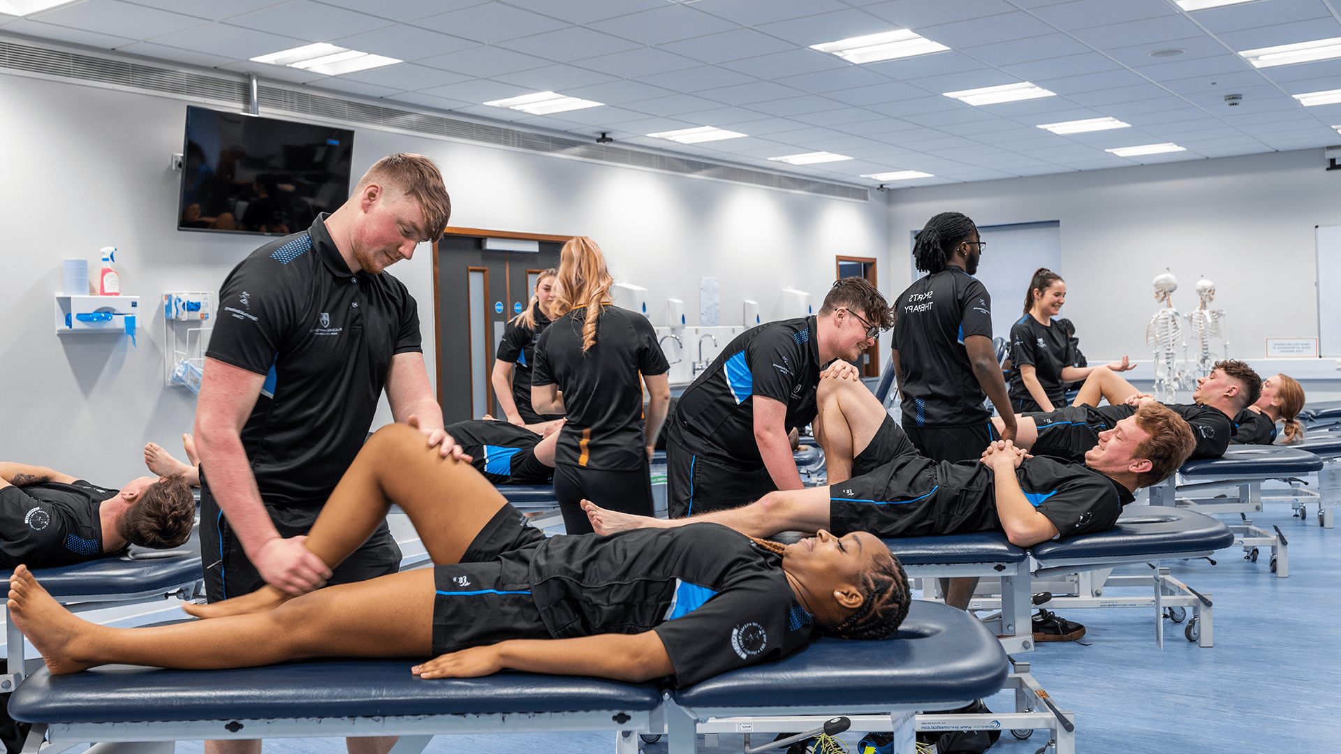 Sports Therapy students in uniform attending to a fellow student laying on a bed