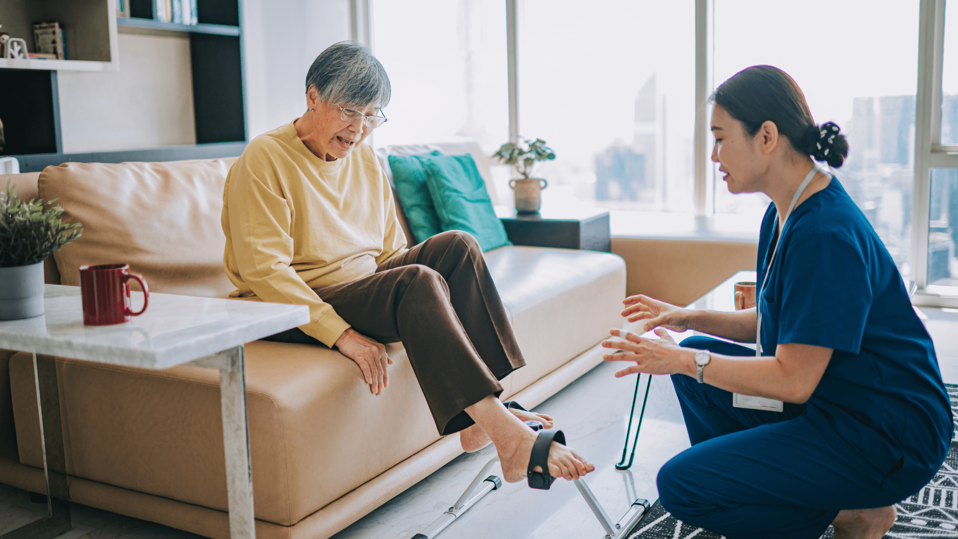 An occupational therapist kneeling down as a patient is sat on a sofa doing some foot exercises.