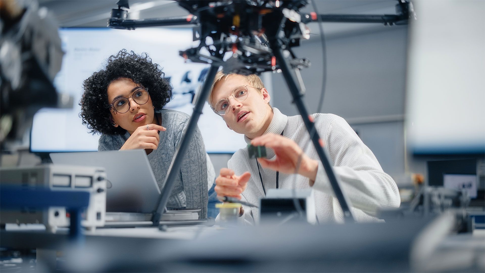 Two professionals in a computing lab examining an electronic device on legs