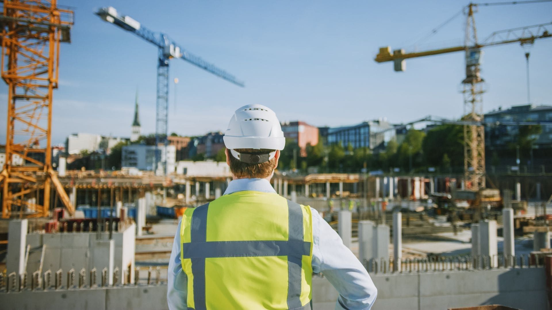 A builder with a hard had and high vis jacket on, looks over a construction site
