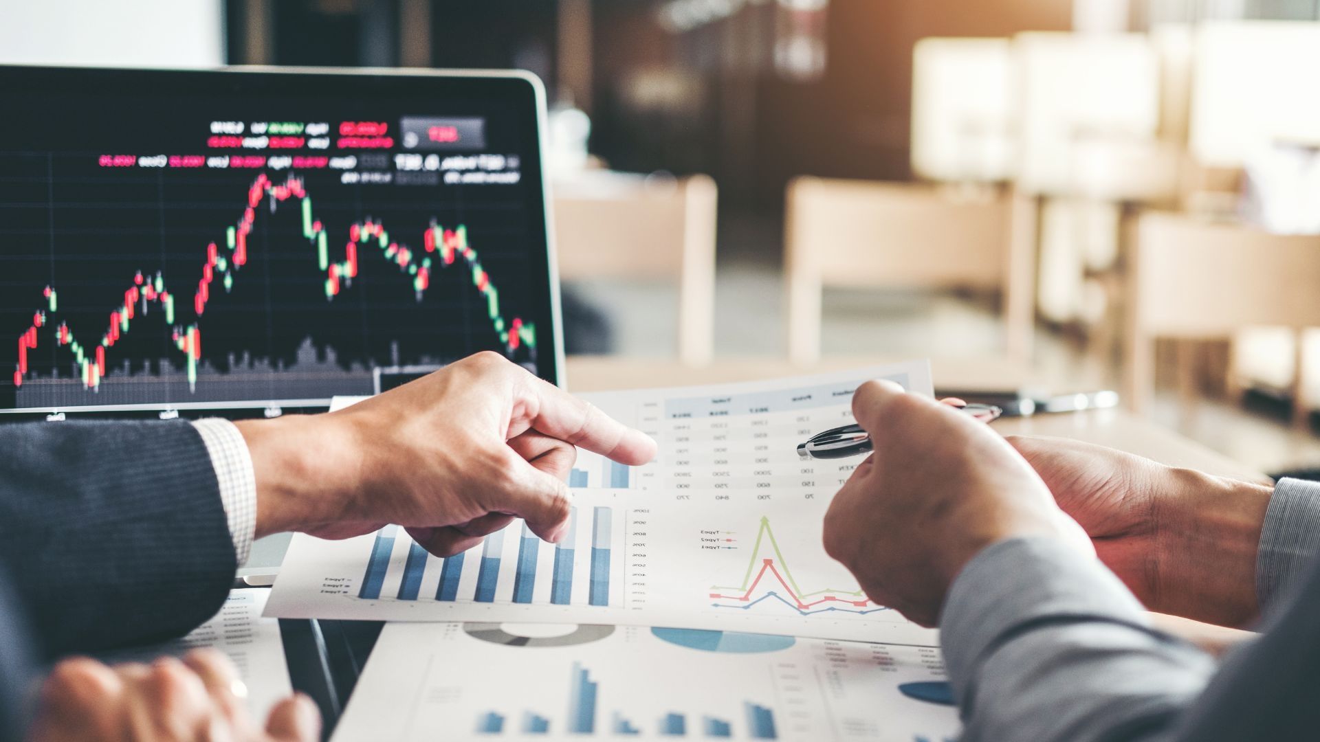 Two hands looking at data on a bit of paper with a laptop in the background.