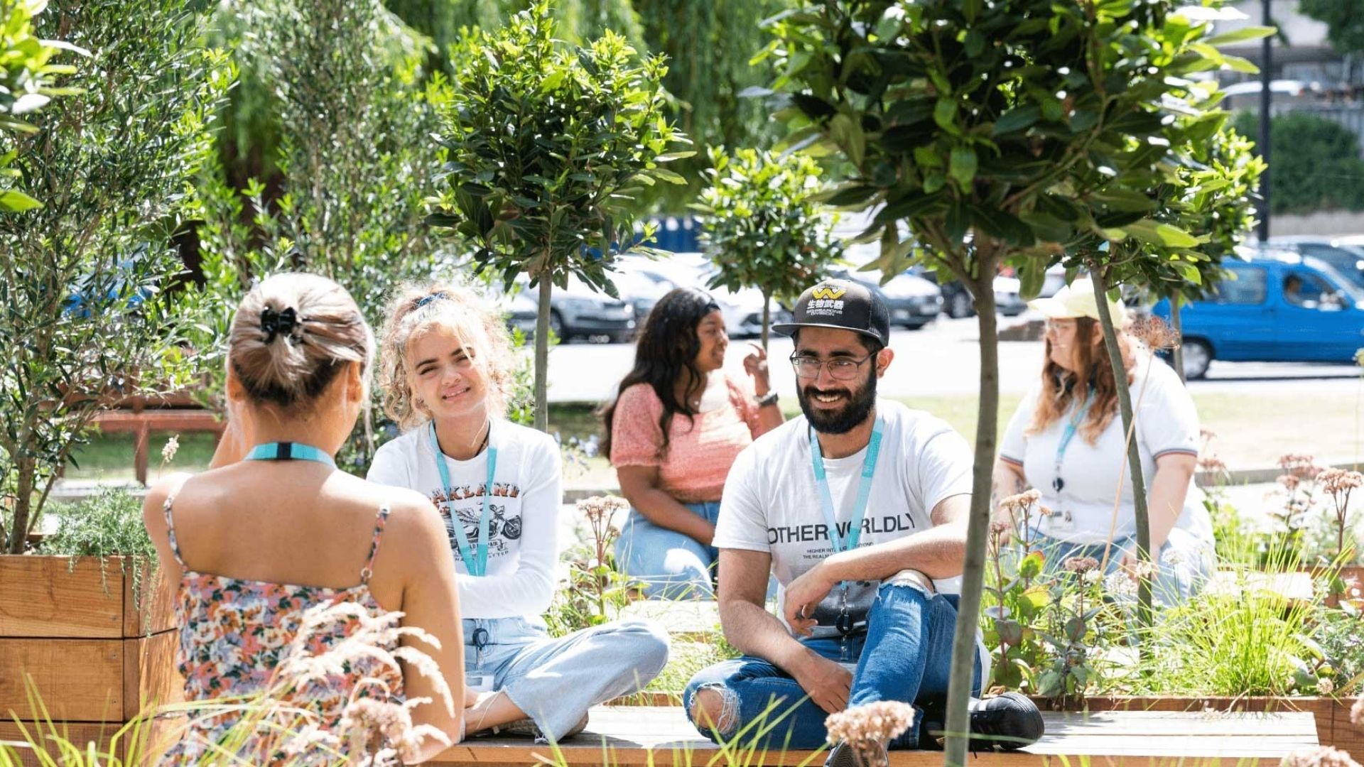 Five BNU students sat on wooden benches in amongst trees on concourse in the sunshine