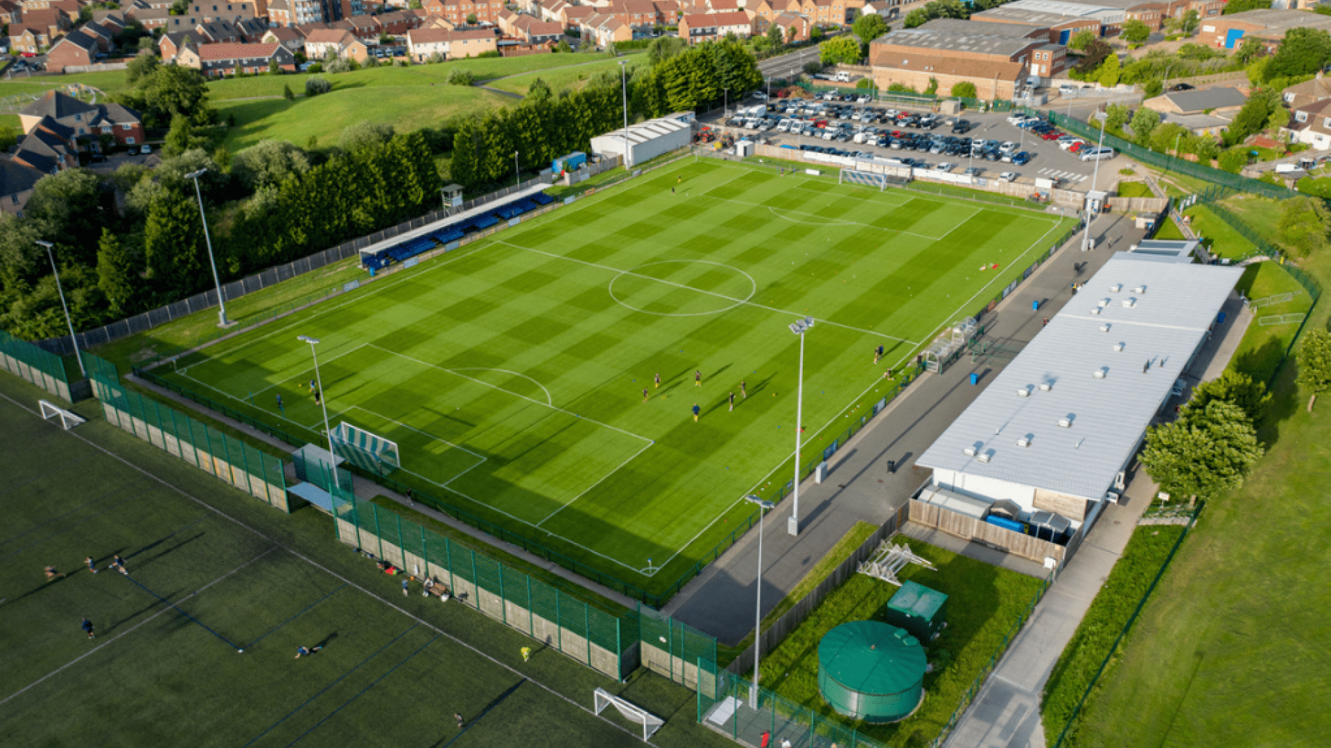 An sunny aerial drone shot of a football pitch surrounded by houses.