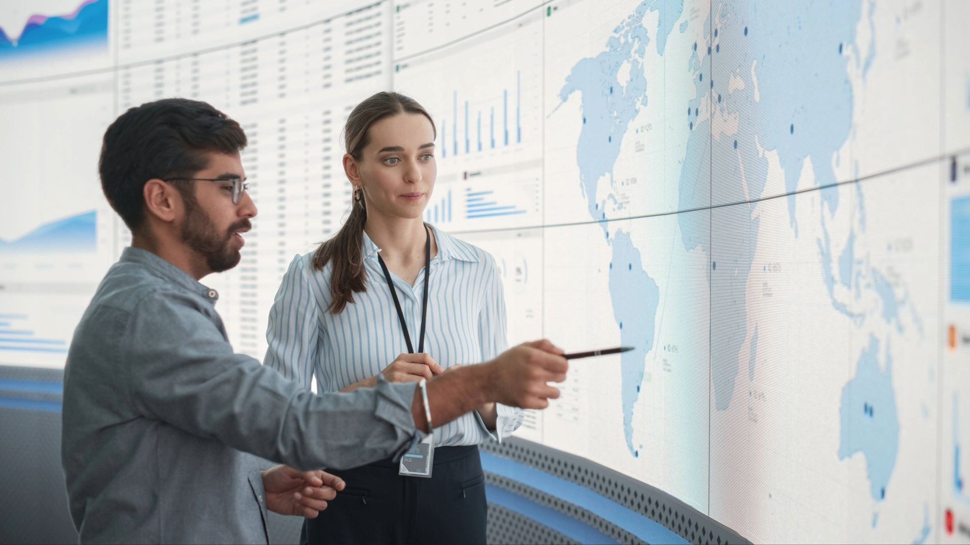 two people talking in front of a digital screen with a map, graphs and charts
