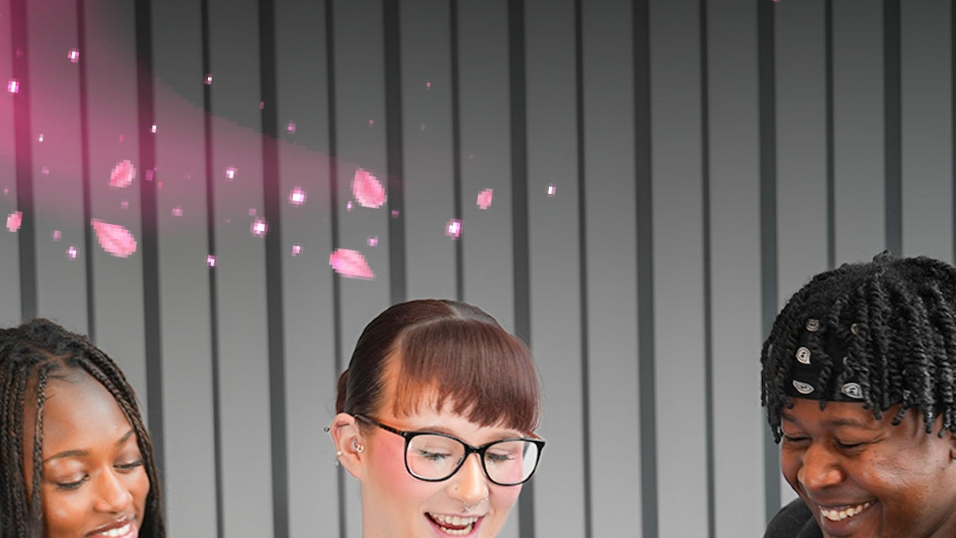 Three students sat on a sofa looking at one phone against a striped wall.