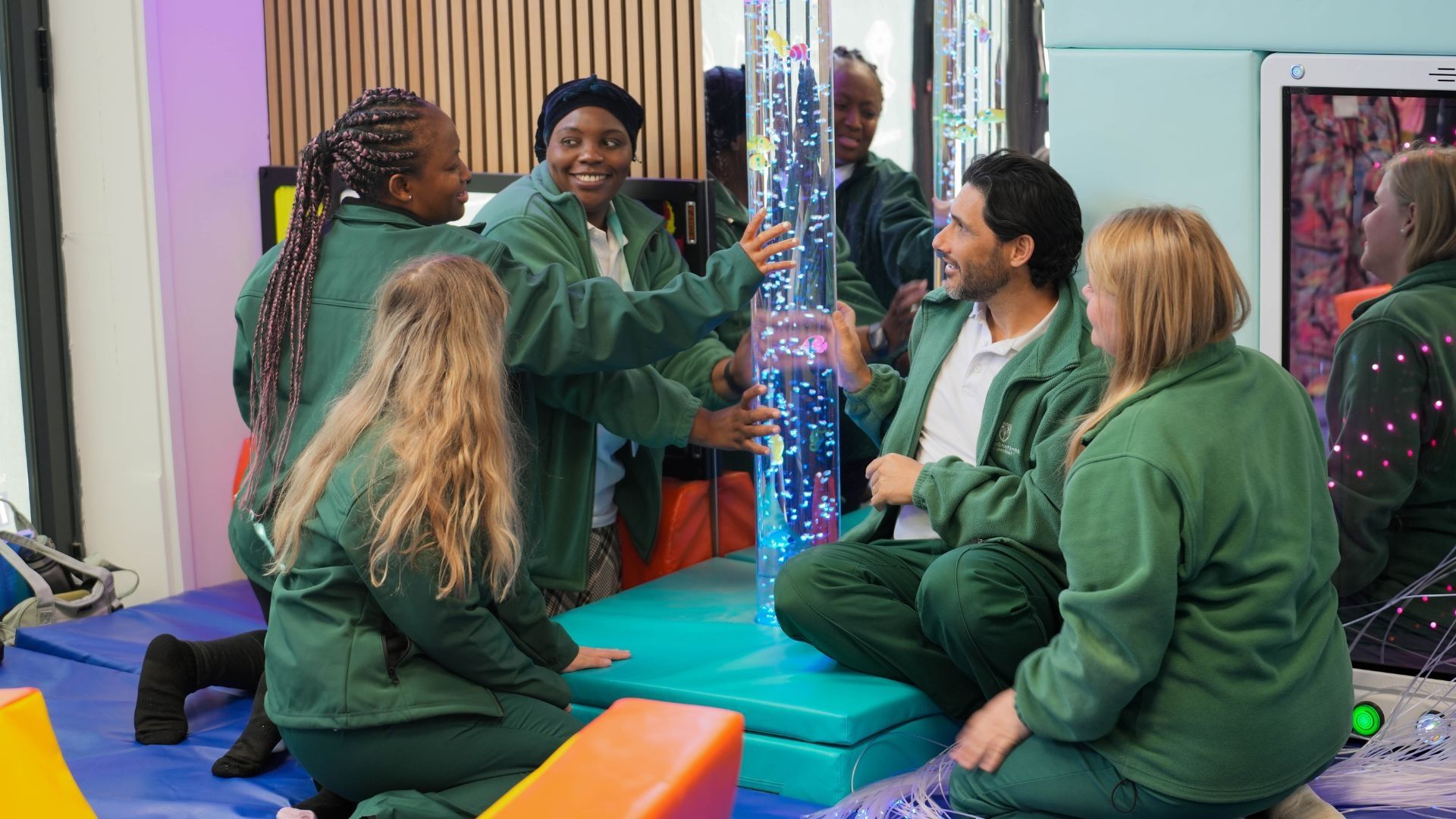 Four Occupational Therapy students in sensory room kneeling down looking at a water tube with lights in.