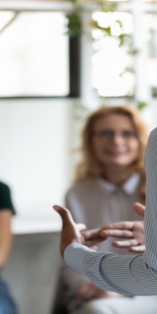 A woman with her back to the camera delivers a speech to three other females