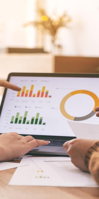 two people sat next to each other pointing at a laptop with bar graphs on