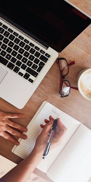 aerial view of a woman sat at a table making notes next to her laptop