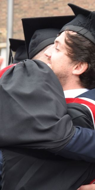 two students hugging in graduation robes