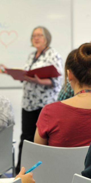 Two female students facing the front of a classroom sat on chairs