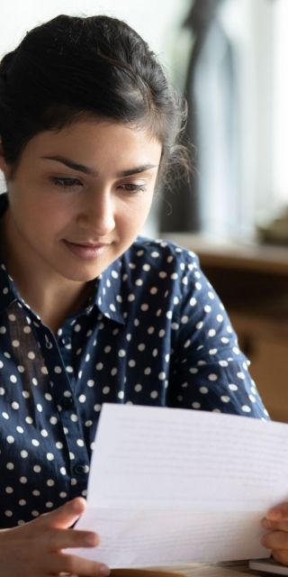Student reading a piece of paper at a desk next to a laptop