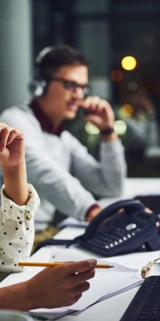 Female on headset phone writing down notes. Man in background on phone