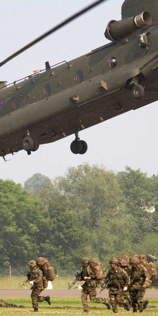 Military chinook flying with soldiers on the ground ready to disperse 