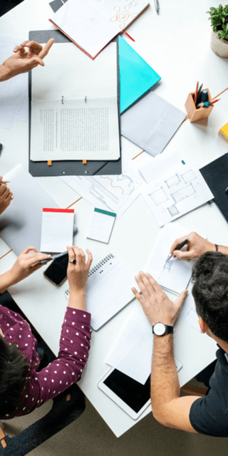 An aerial view of a table with 5 students sat around it looking and discussing at meeting notes 