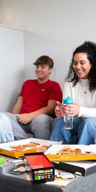 Four students eating pizza in a lounge area in Windsor House accommodation