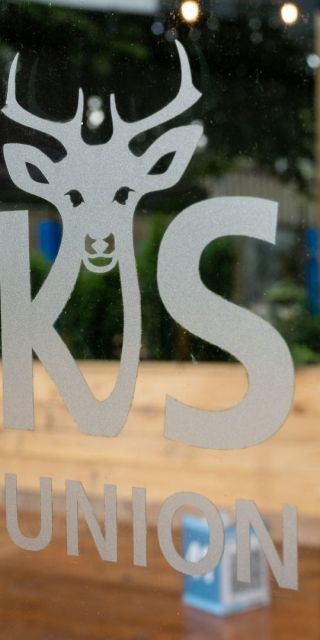 Bucks Students' Union logo on a pane of glass which has an outdoor wooden seating area behind it