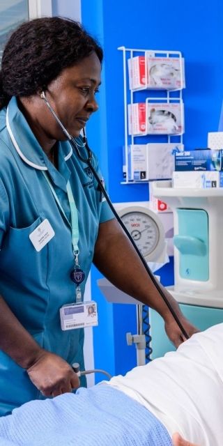 A Nursing student stood up leaning of a hospital bed which has a male dummy in it