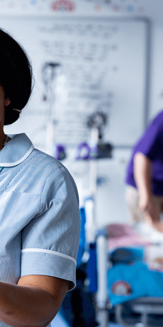 A female student nurse looking at her notes whilst a lecturer assists to a dummy patient in the background