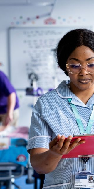 A student nurse in uniform stood in a simulation ward looking down at a tablet screen