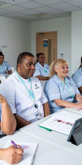 Eight nursing students sat in their uniform in a classroom facing the front of the room with textbooks open