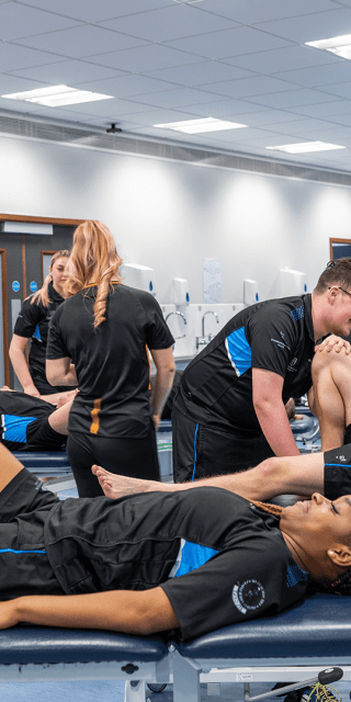 Sports Therapy students in uniform attending to a fellow student laying on a bed
