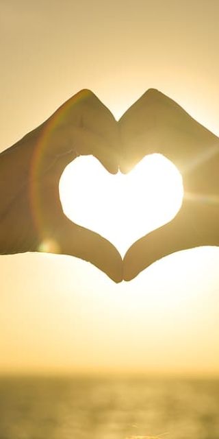 Image of two hands together to make a heart shape in front of sun