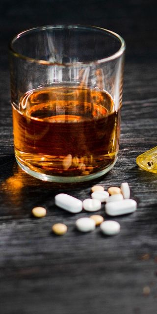 glass of whiskey, ashtray, cigarettes, pills and drug paraphernalia on a table