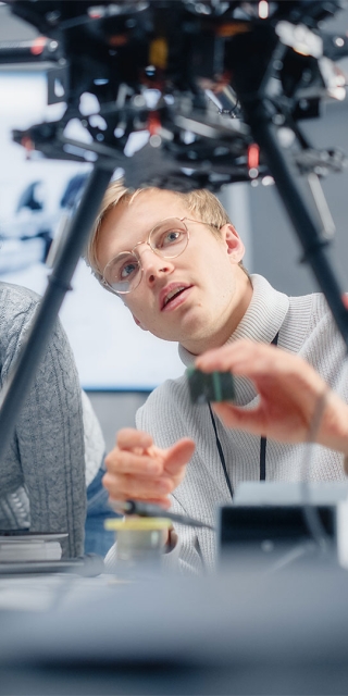 Two professionals in a computing lab examining an electronic device on legs