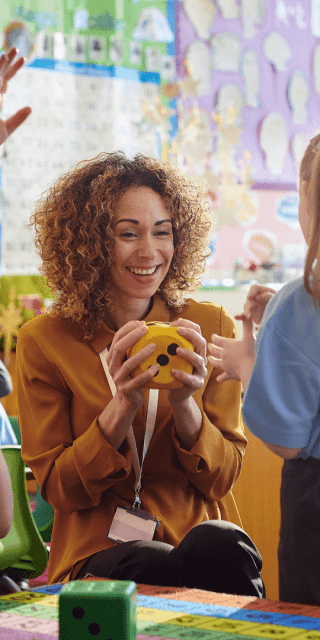 Primary School students stood talking to their teacher in a classroom.