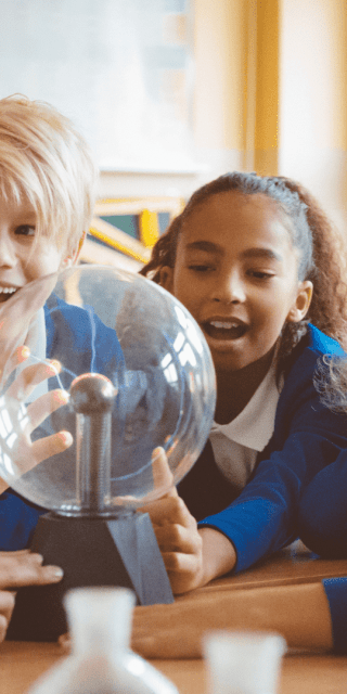 Four primary school children sat around a table smiling toward their teacher.