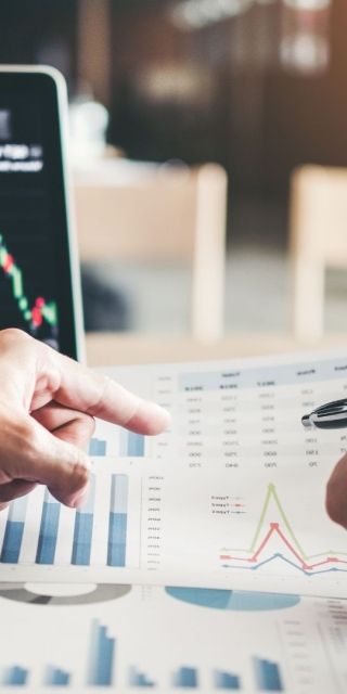 Two hands looking at data on a bit of paper with a laptop in the background.