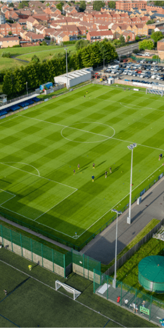 An sunny aerial drone shot of a football pitch surrounded by houses.