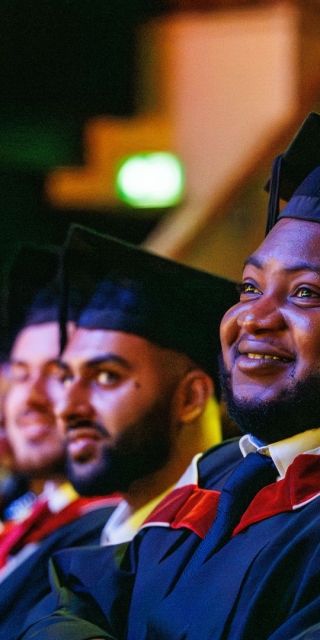 Students sat down smiling in a theatre as they watch fellow students graduate.